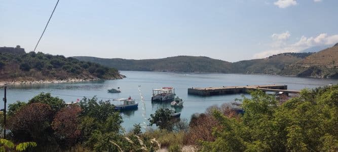 Barquitos sobre el agua en la playa de Porto Palermo con el castillo al fondo
